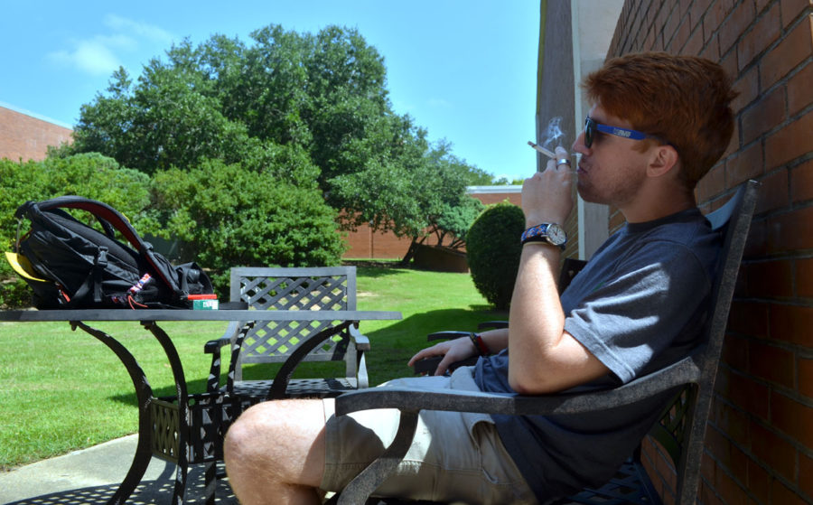 Senior Jay Spear stops to enjoy a cigarette after walking through Southern Miss campus on Sunday.  He sits in the shade in one of the designated smoking areas outside Joseph Greene Hall. - Aaron J. Stewart