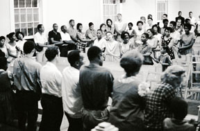 From the Randall (Herbert) Freedom Summer Photographs. Photograph (positive image of a negative) of local people and volunteers crossing arms and joining hands to sing the anthem of the civil rights movement, We Shall Overcome at True Light Baptist Church in Hattiesburg, Mississippi, as part of Freedom Summer, 1964. This photo was probably taken after the performance of Martin Dubermans play In White America by the Free Southern Theater performers.