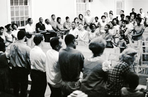 From the Randall (Herbert) Freedom Summer Photographs. Photograph (positive image of a negative) of local people and volunteers crossing arms and joining hands to sing the anthem of the civil rights movement, "We Shall Overcome" at True Light Baptist Church in Hattiesburg, Mississippi, as part of Freedom Summer, 1964. This photo was probably taken after the performance of Martin Duberman's play "In White America" by the Free Southern Theater performers.