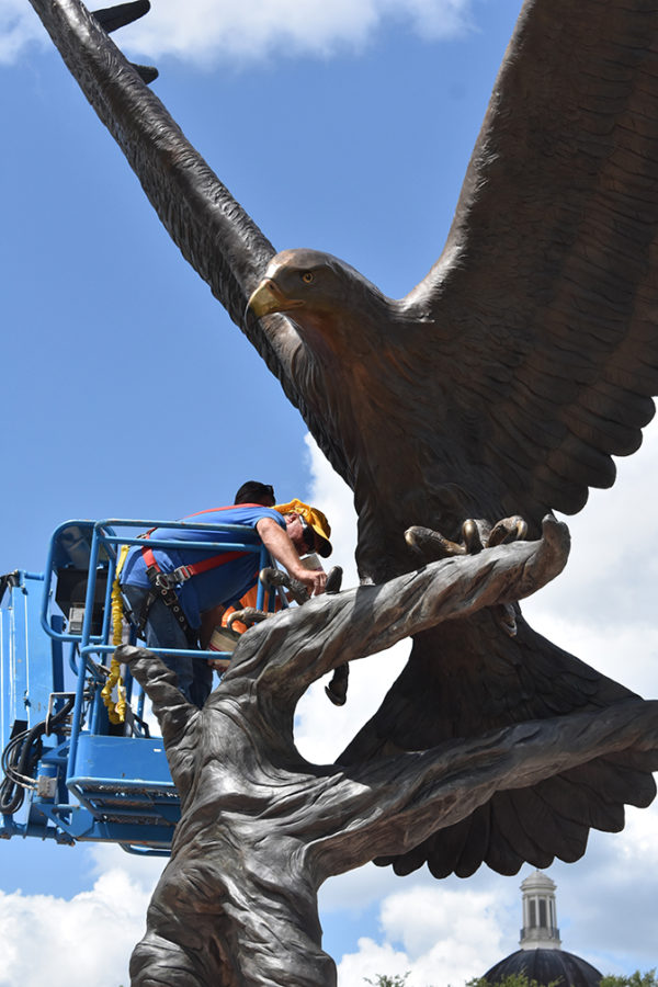 Stephen Miller and Lyman Greer clean and wax the golden eagle statue at the front of campus.