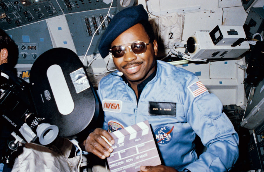 S84-27219 (3-11 Feb 1984) --- Astronaut Ronald E. McNair, 41-B mission specialist, doubles as director for a movie being produced aboard the Earth-orbiting Space Shuttle Challenger.  McNairs name tag (Cecil B. McNair) and beret and slate are all humorous props for application of a serious piece of cargo on this eight day flight - the Cinema 360 camera.  Two of the cameras were carried aboard the Challenger to provide a test for motion picture photography in a unique format designed especially for planetarium viewing.  This camera was located in the crew cabin area and a second was stowed in a getaway special (GAS) canister in the payload bay.  The other camera recorded extravehicular activity (EVA) of the flights other two mission specialists, Astronauts Bruce McCandless II and Robert L. Stewart.