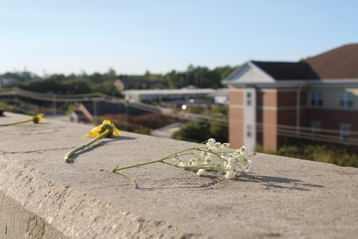 Flowers are lined along the edge of the fifth floor at the 4th Street Parking Garage, where a student tragically died on the night of Sept. 28. Students have gathered to mourn and express condolences, devastated by the loss.