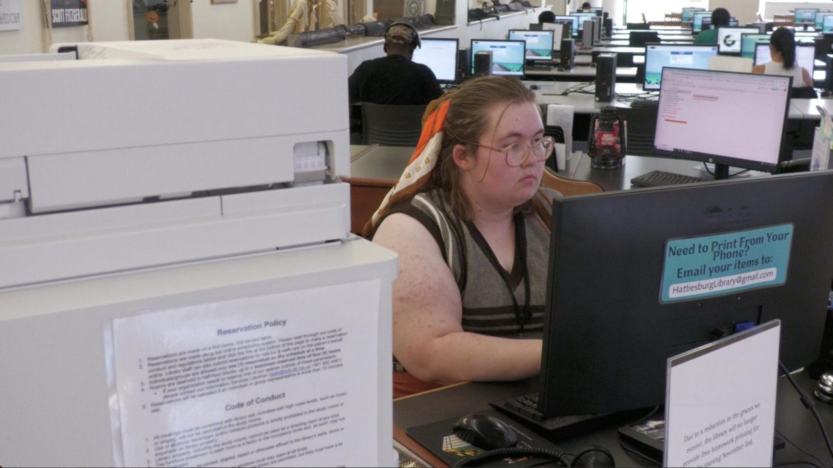 Library staff member Kelly Eubanks is doing work at her desk, with a sign displaying future changes.